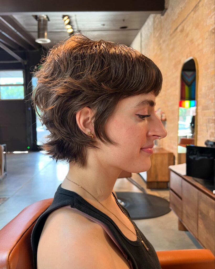 A woman with a short feathered tomboy pixie shag haircut with soft layers and natural volume.