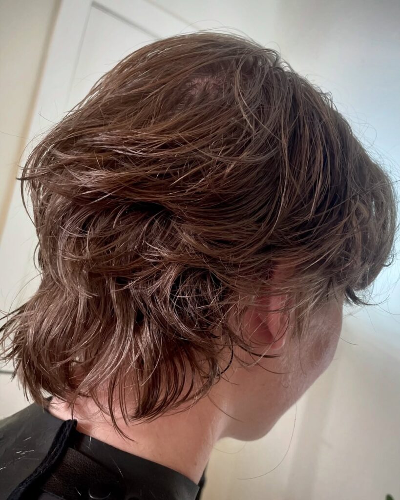 A woman with a short layered tomboy mullet featuring soft texture and longer length at the back.