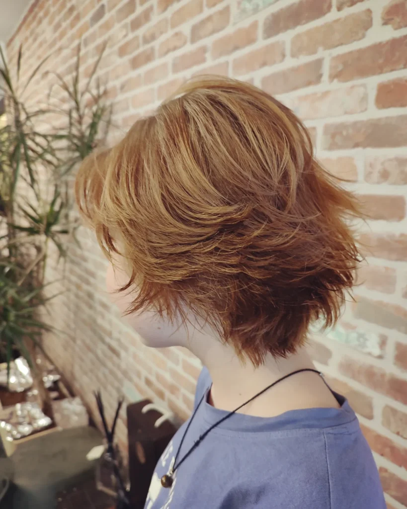 A woman with a short layered copper tomboy shag haircut with feathered texture and soft volume.