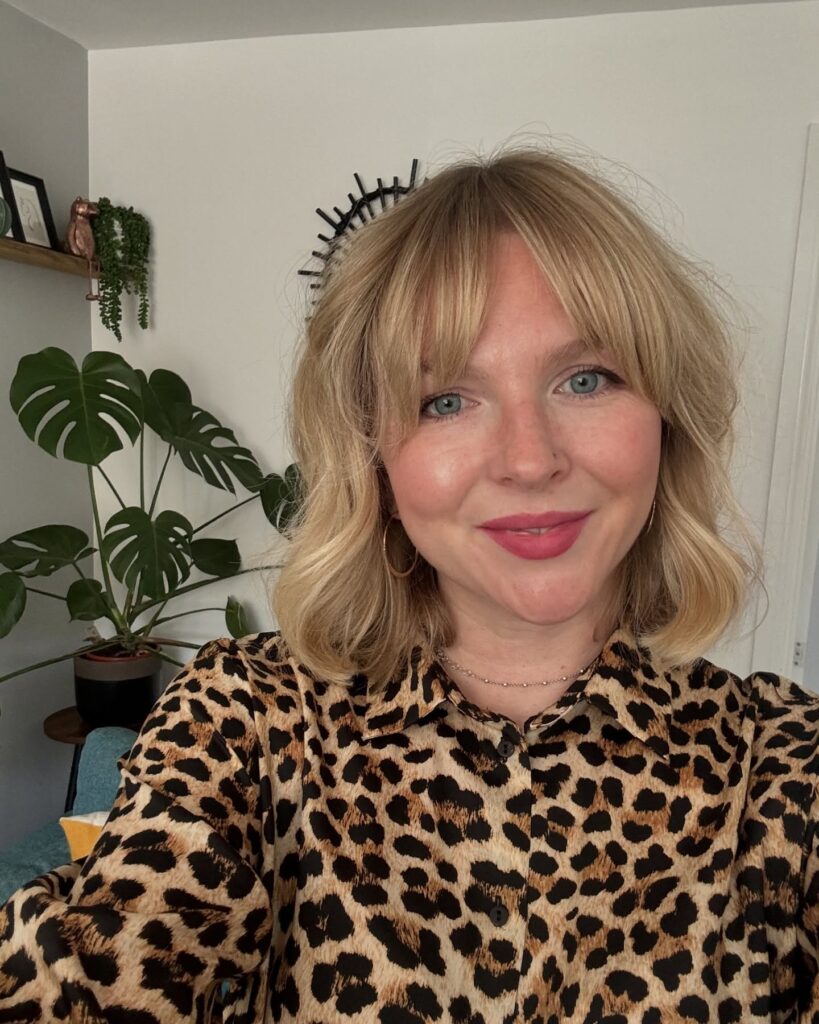 Soft blonde bob with loose waves and full airy bangs framing the face.