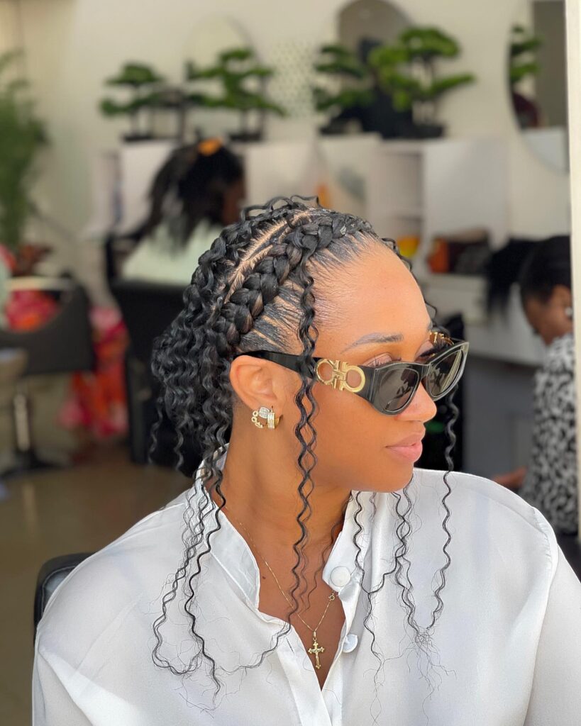 Medium cornrows with loose curly strands framing the face in a half up style.