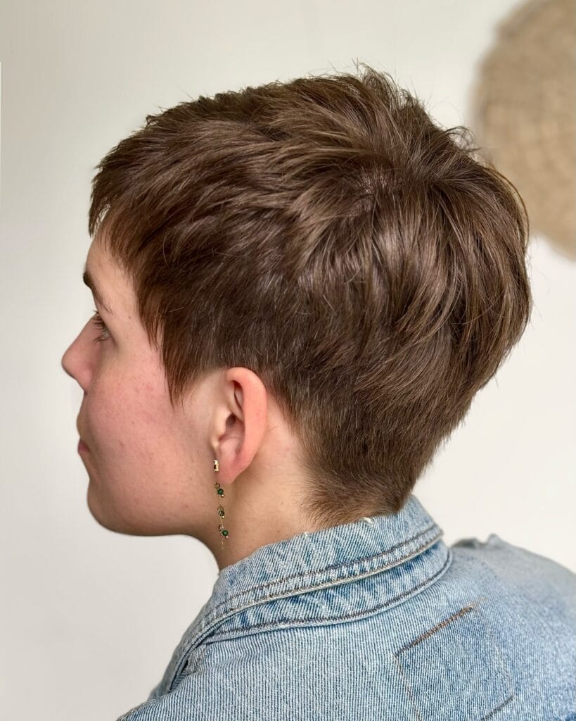 A woman with a short layered tomboy crop haircut featuring a tapered back and softly textured brown hair.