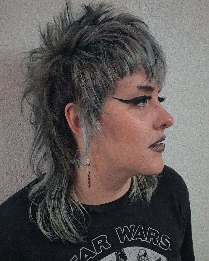 A woman with a textured tomboy shag mullet featuring choppy layers, longer back length, and ashy gray hair color.