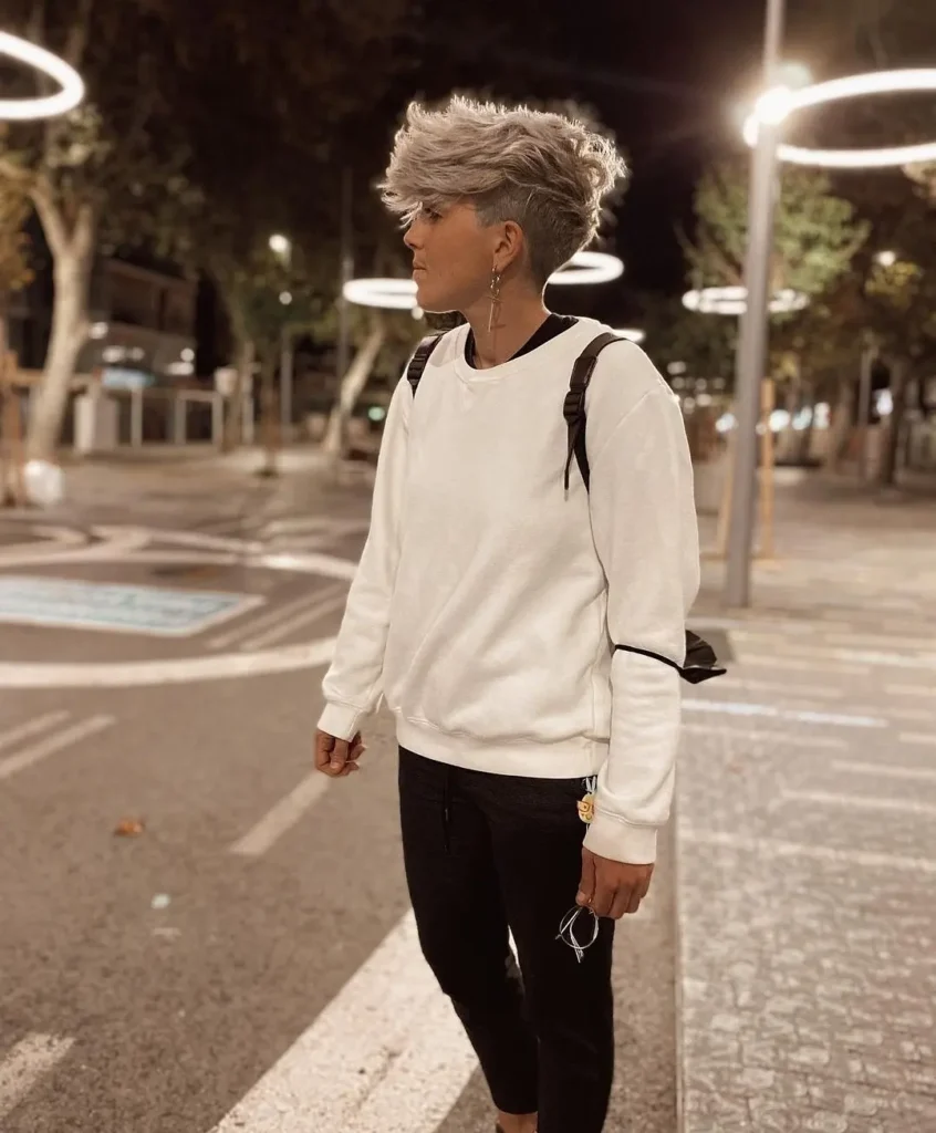 A woman with a voluminous tomboy undercut featuring short faded sides and a textured blonde top styled upward.