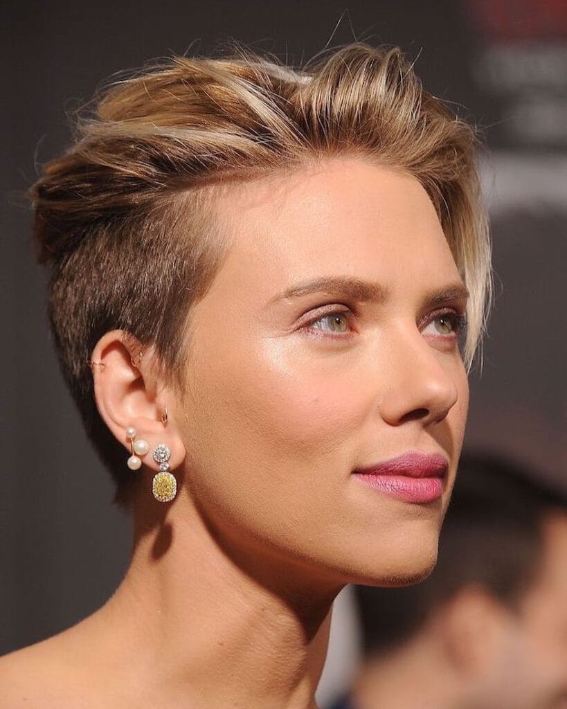 A woman with a sleek blonde undercut pixie haircut with volume on top and closely trimmed sides.