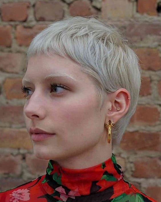 A young woman with a short platinum blonde textured crop haircut and undercut sides.