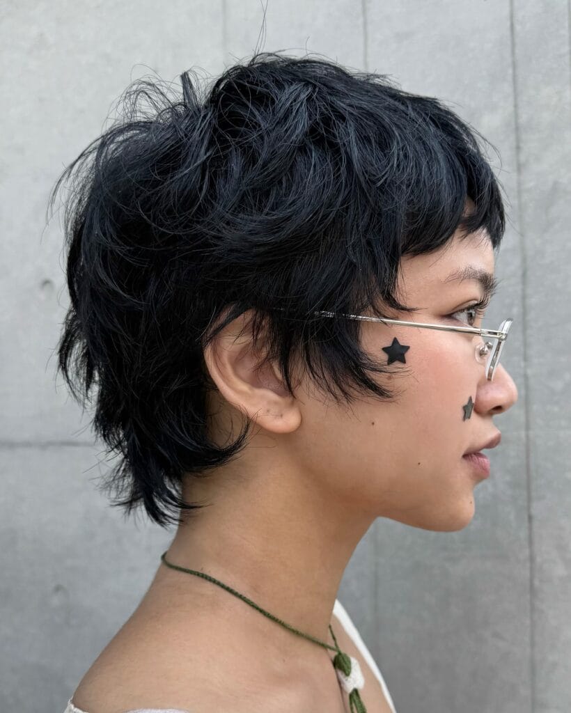 A young woman with a short black choppy tomboy shag haircut with a soft mullet shape and layered texture.