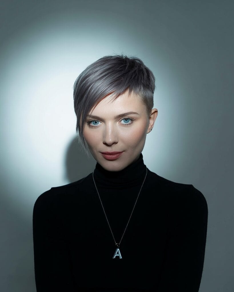 A young woman with a sleek asymmetrical silver pixie haircut with short sides and longer front layers.