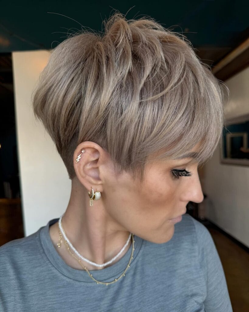 A woman with a beige blonde undercut pixie haircut with feathered layers and side swept volume.