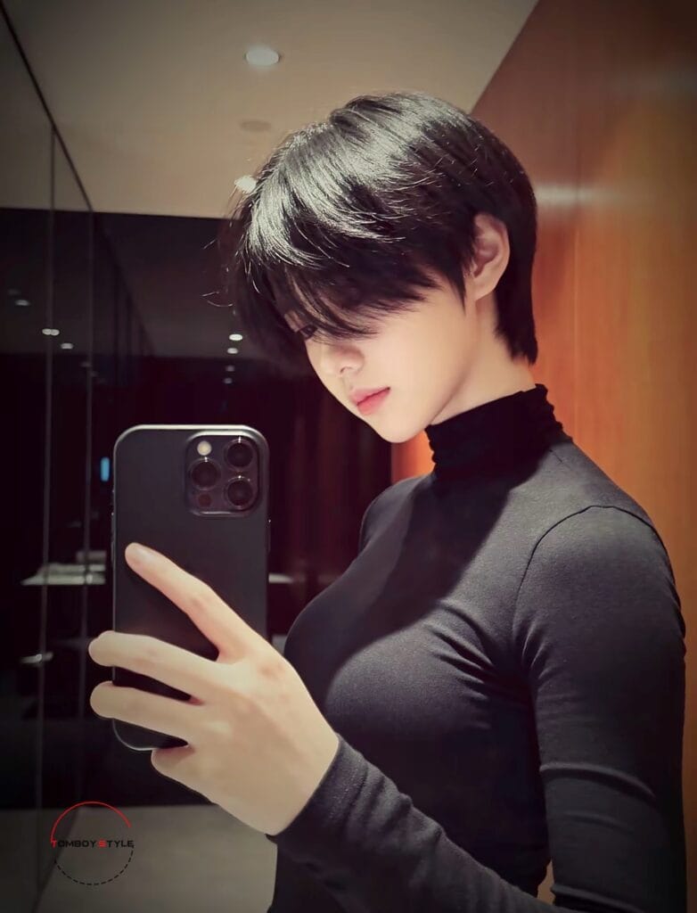 A young woman with a sleek black tomboy haircut featuring short layers and a long fringe covering part of the face.