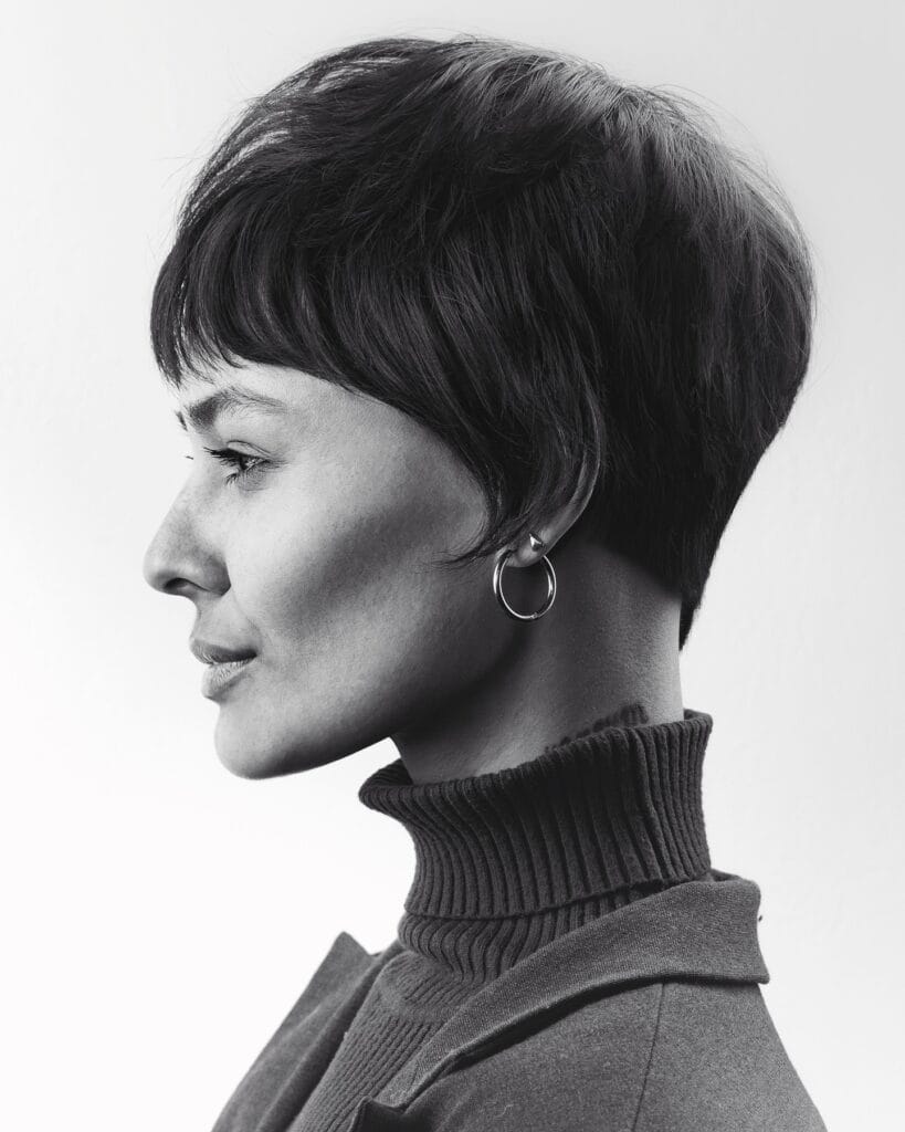 A woman with a classic short dark pixie haircut featuring soft layers and a neat fringe.