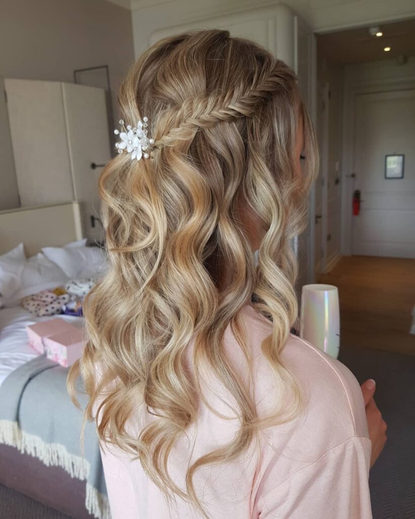 Long blonde wavy hair styled in a soft braided half up hairstyle with a delicate hair accessory.