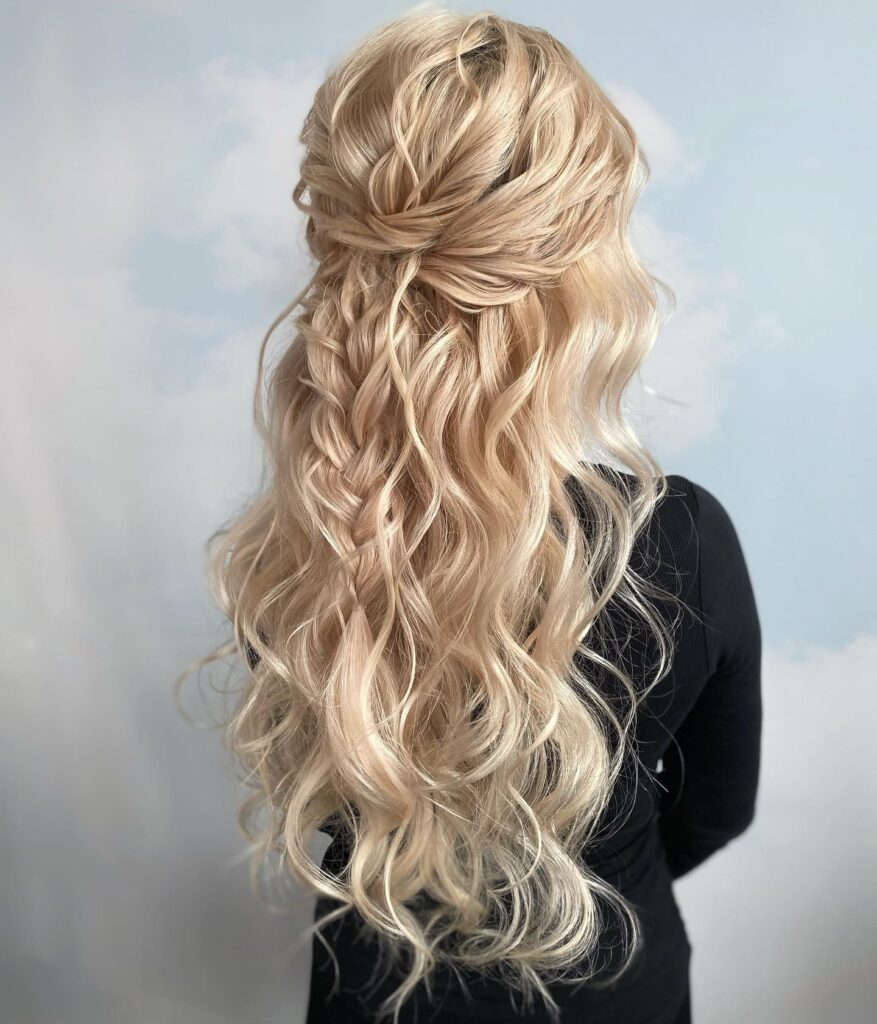 Long blonde wavy hair styled in a loose twisted half up hairstyle with soft curls.