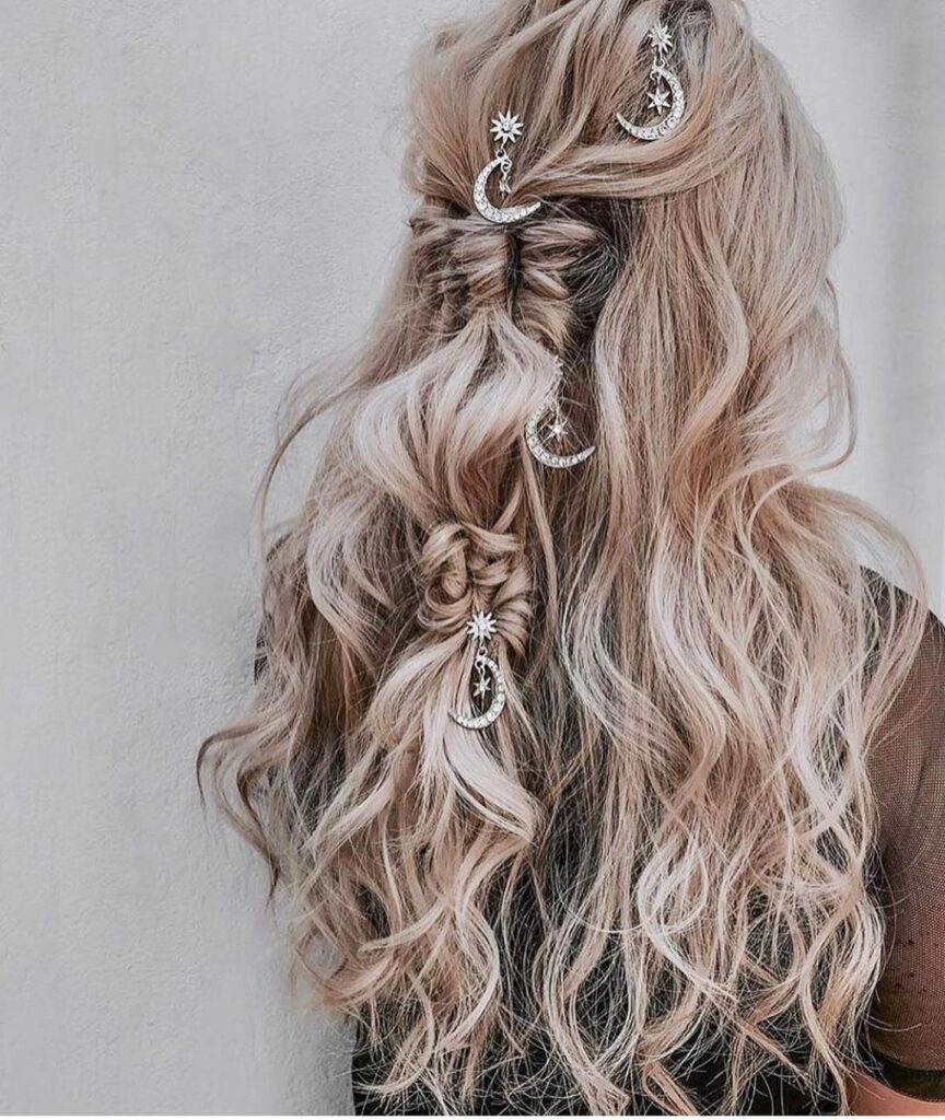 Long wavy blonde hair styled in a half up twist with star and moon hair accessories.