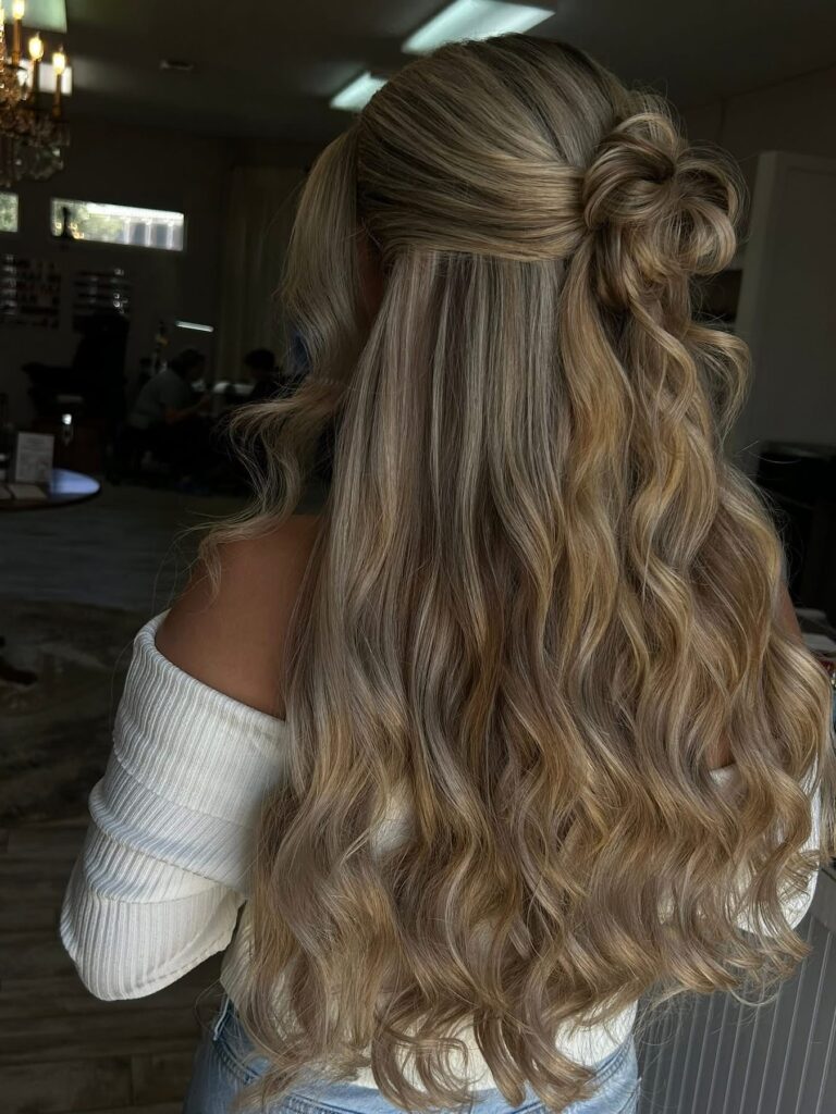 Long wavy blonde hair styled in a half up twisted knot with soft loose curls.