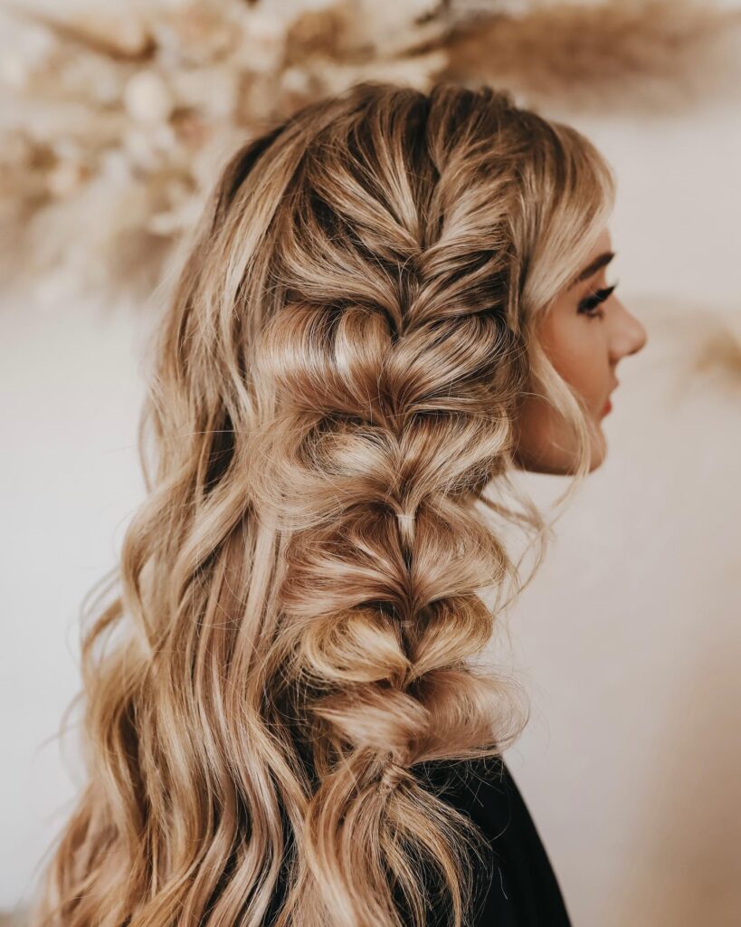 Long curly blonde hair styled in a voluminous boho side braid with loose waves.