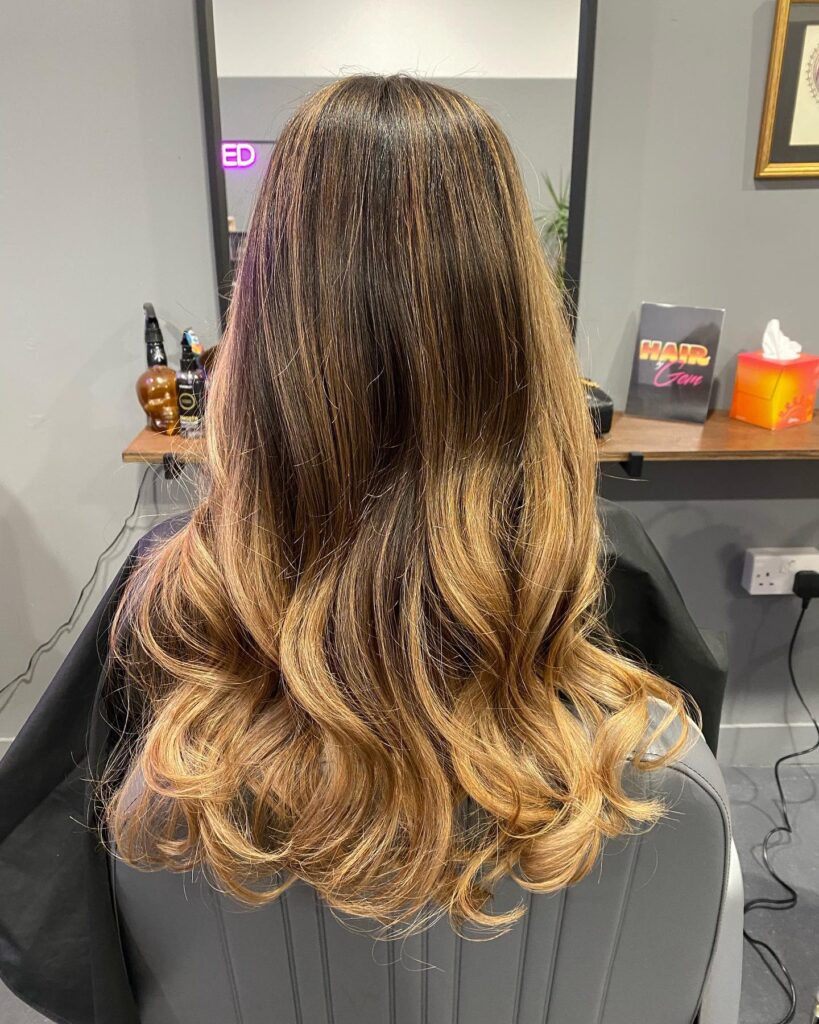 Long layered hair with soft loose curls and blended highlights.