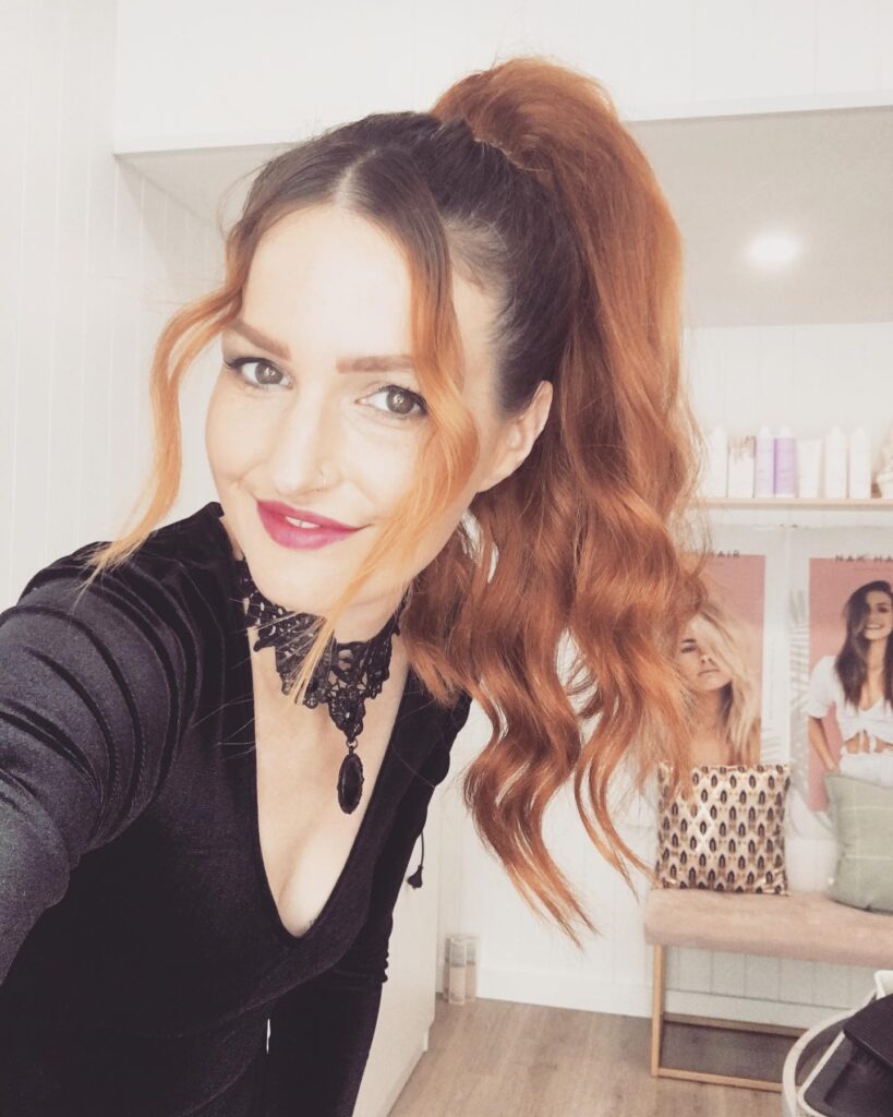 Long curly hair styled in a high ponytail with soft waves and loose face framing strands.