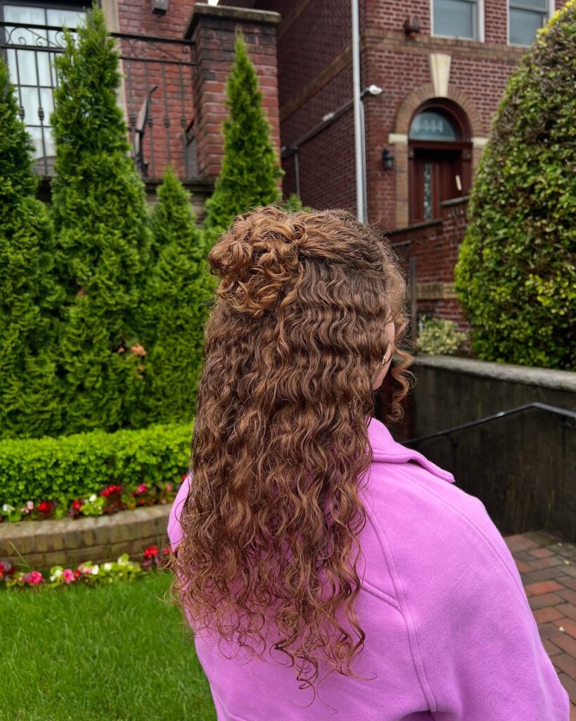 Long curly hair styled in a half up ponytail with natural volume and loose curls.