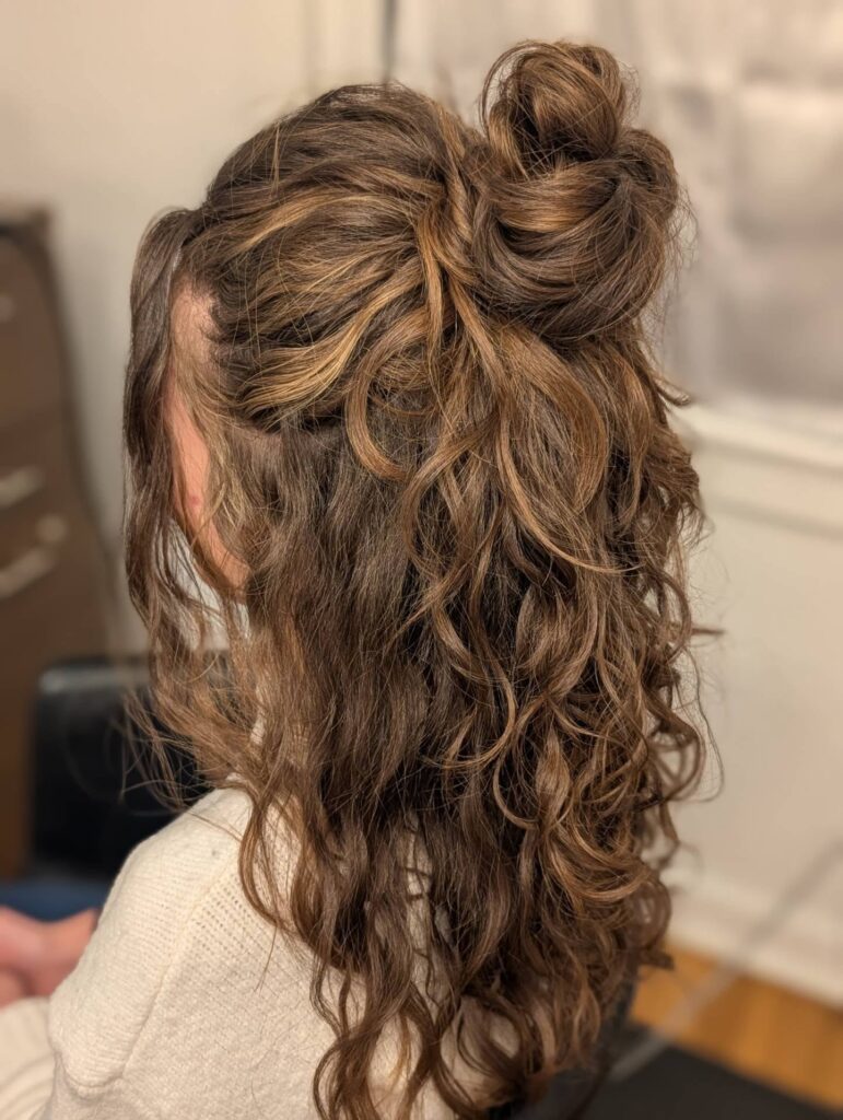 Long wavy curly hair styled in a half up messy bun with loose strands framing the face.