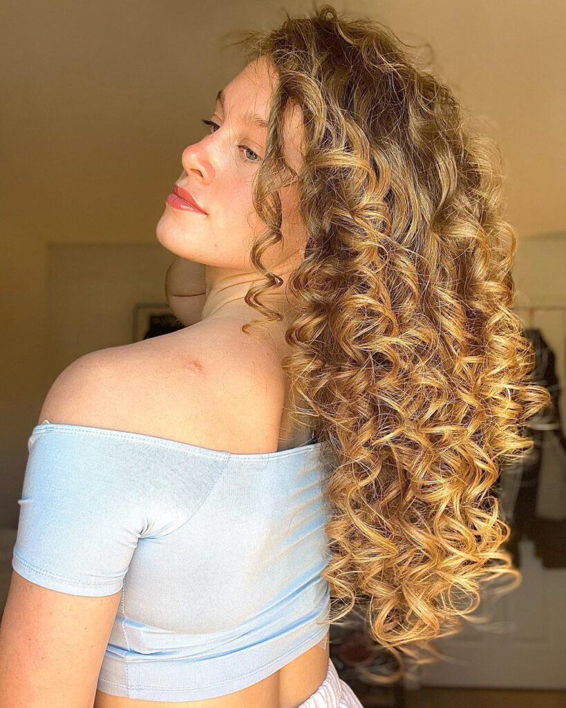 Long curly hair swept to one side with defined bouncy curls and natural shine.