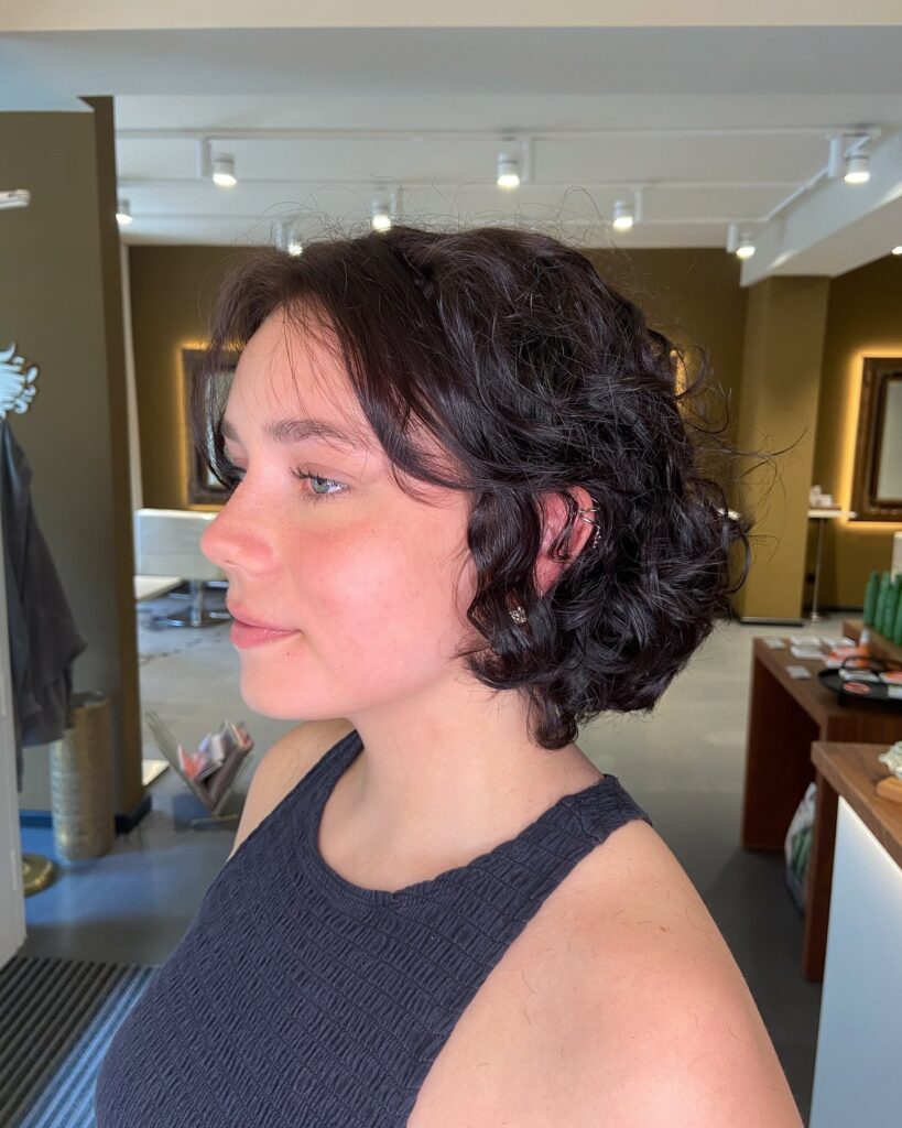 A short dark curly bob with soft face framing curls and a slightly cropped length.