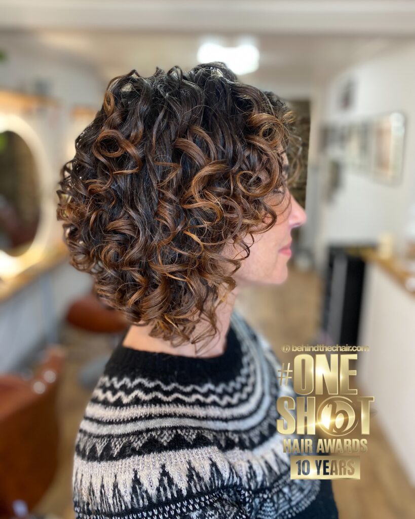 A chin-length curly bob with bouncy curls and warm caramel highlights on a darker base.