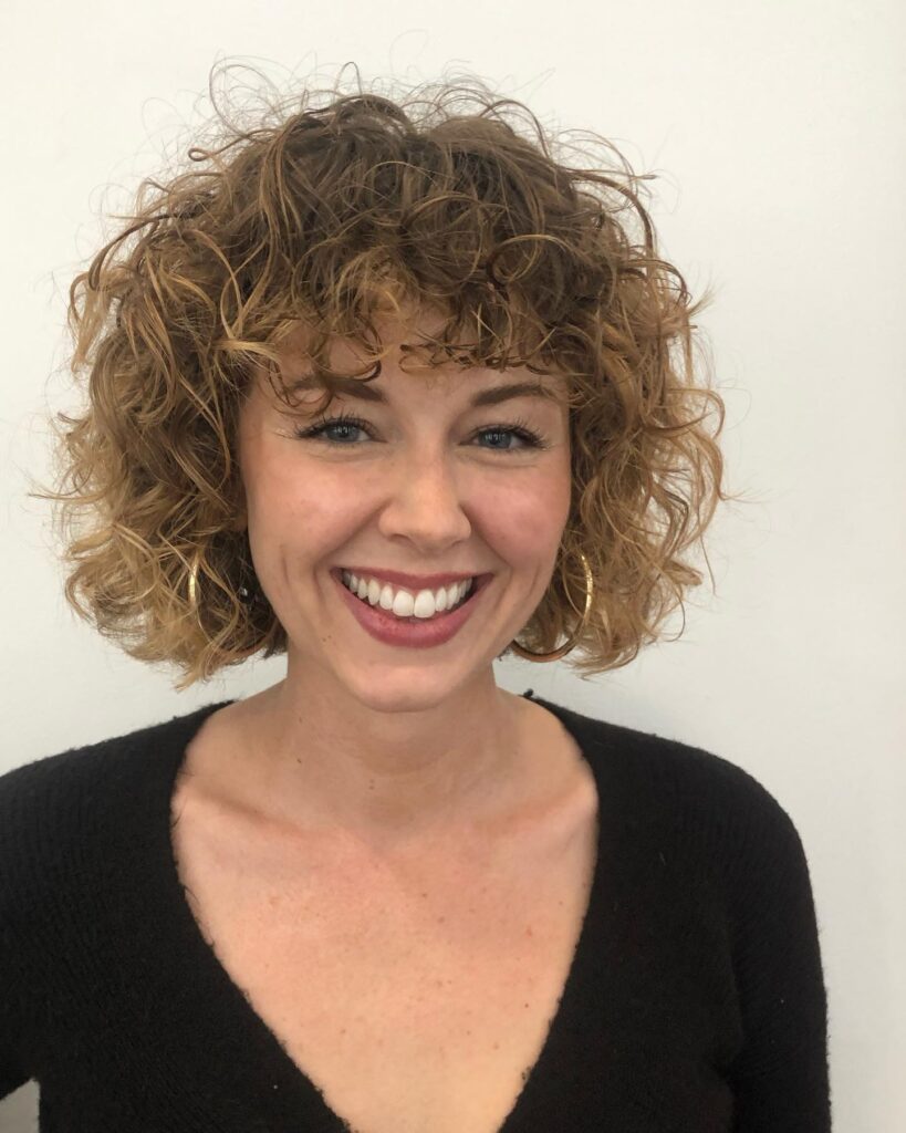 A layered curly bob with a soft fringe and warm golden brown tones.