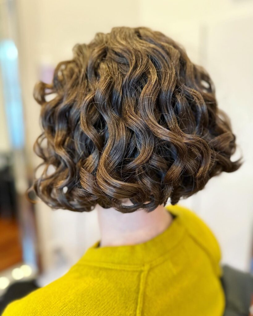 A shiny curly bob with defined curls and soft caramel highlights.
