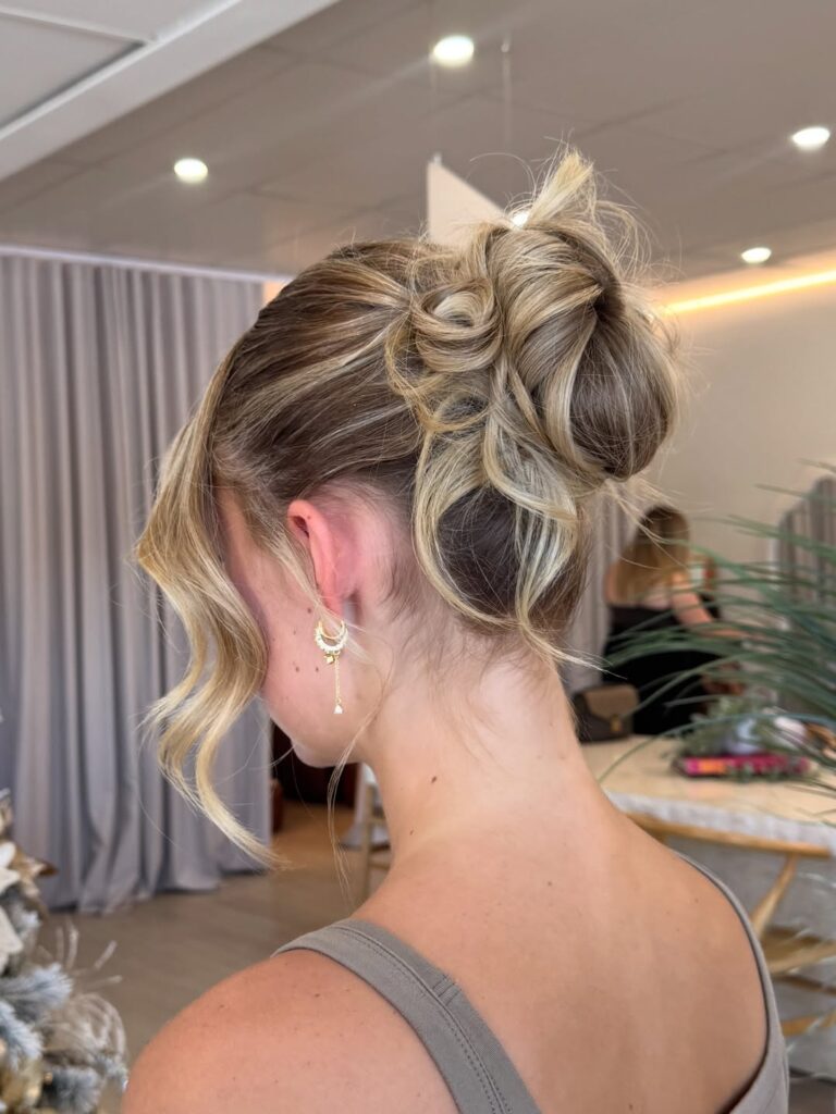 Textured high bun with blonde highlights and a loose curled strand at the front.