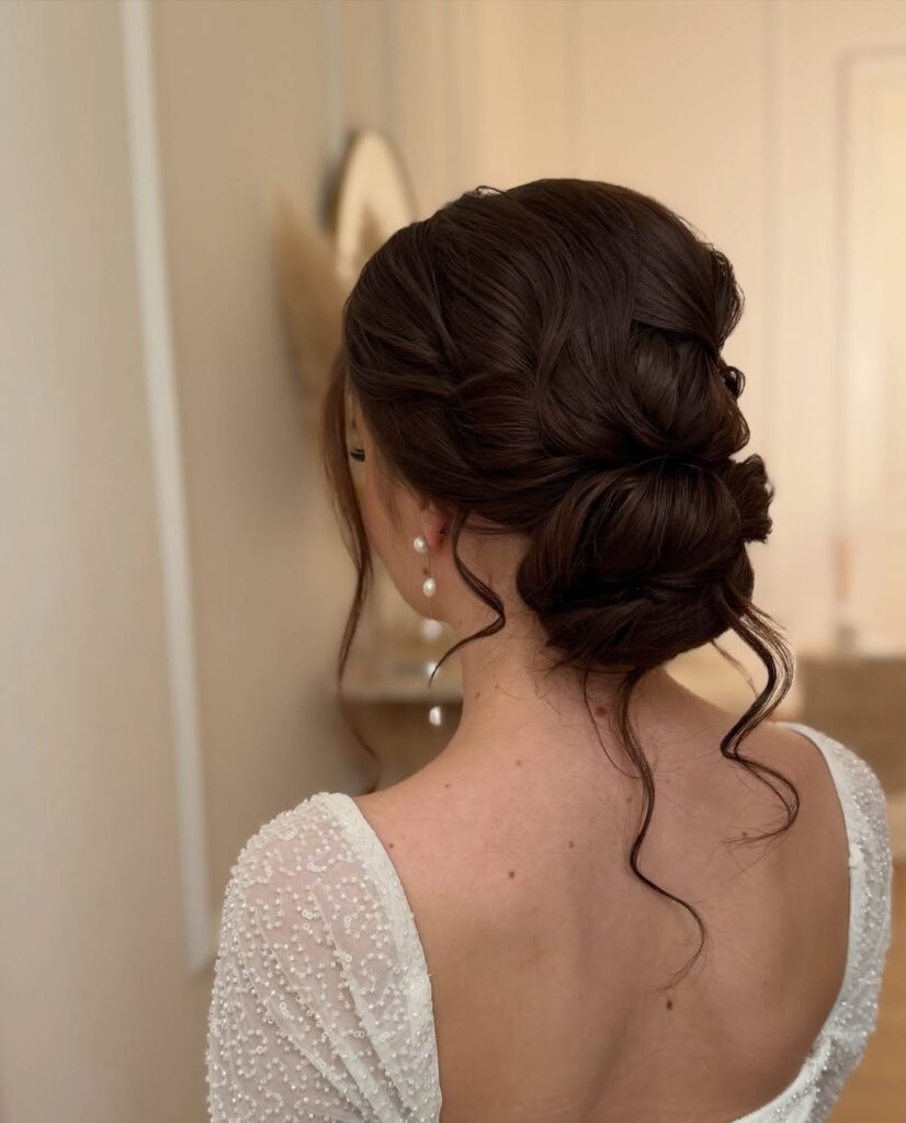 Textured low curly bun with soft twists and loose strands for a romantic finish.