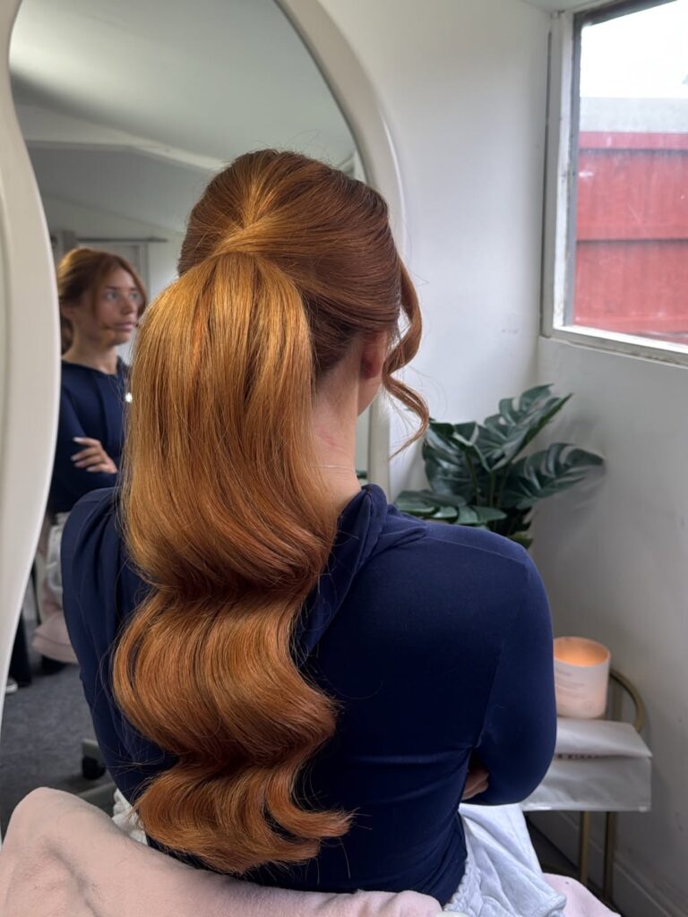 High ponytail with a sleek crown and soft flowing waves in a warm copper tone.