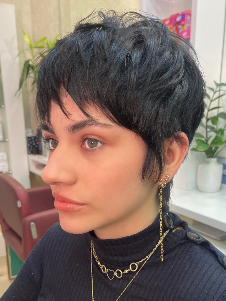 A woman with a short dark textured tomboy pixie haircut and soft wispy bangs framing her face.