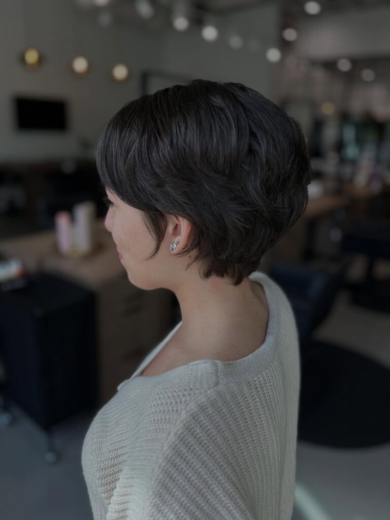 A woman with a sleek rounded tomboy pixie haircut and a softly tapered nape.