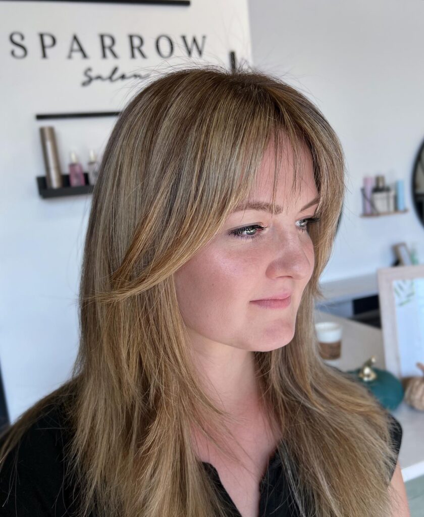 Long layered brunette hairstyle with feathered bangs and soft face framing layers.