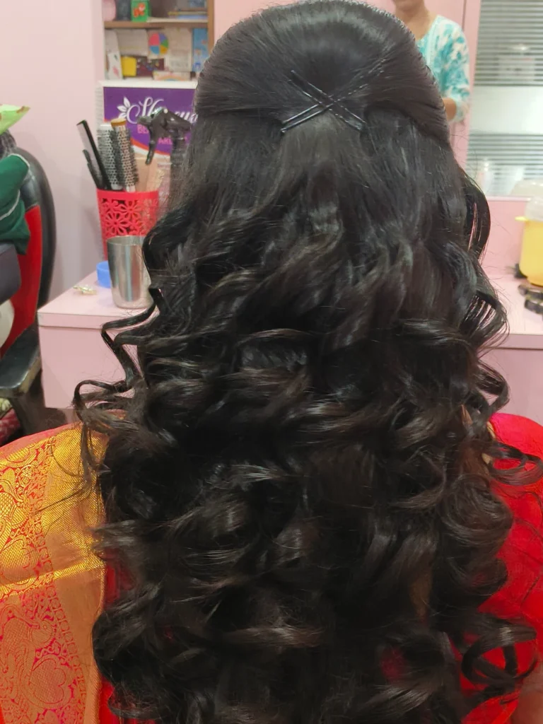 Long dark hair styled in soft curls with a half up pinned section at the back.