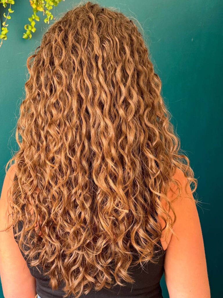 Long light brown curly hair with natural defined texture and soft volume throughout.