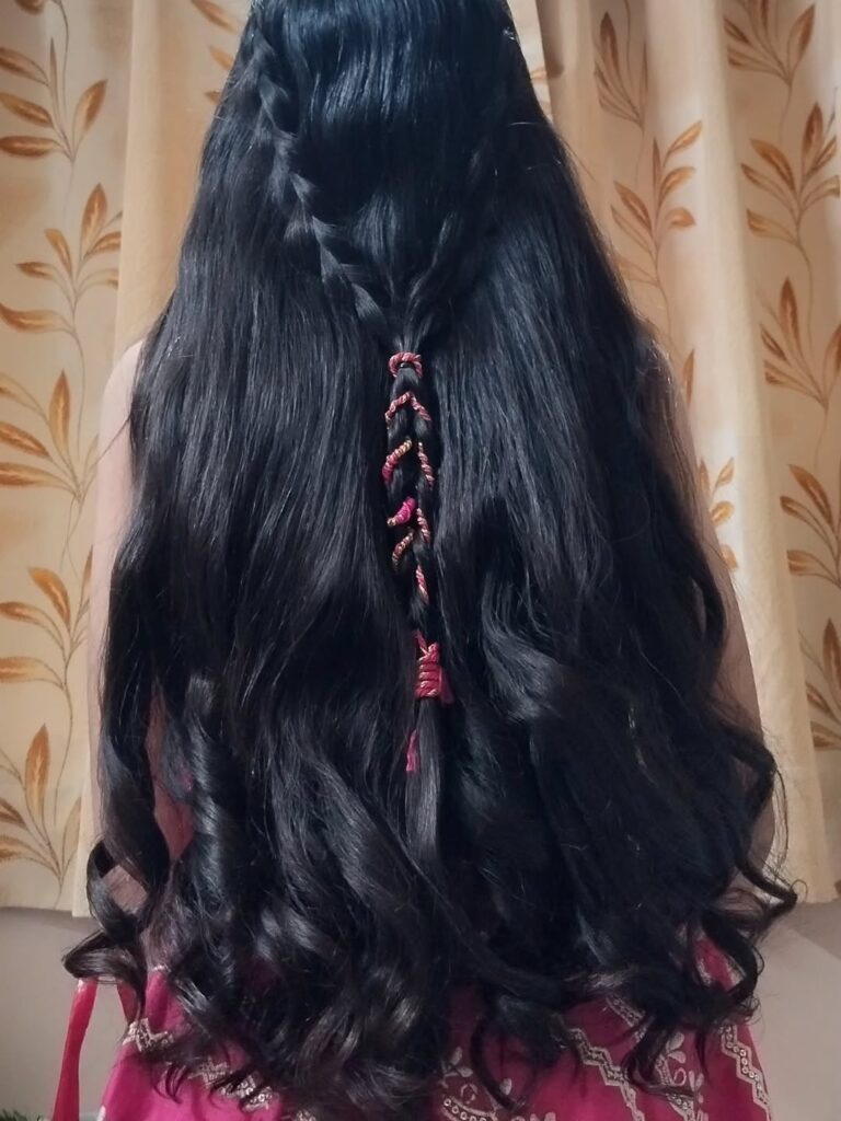 Long black hair styled in loose curls with a sleek half up braid decorated with thread accents.