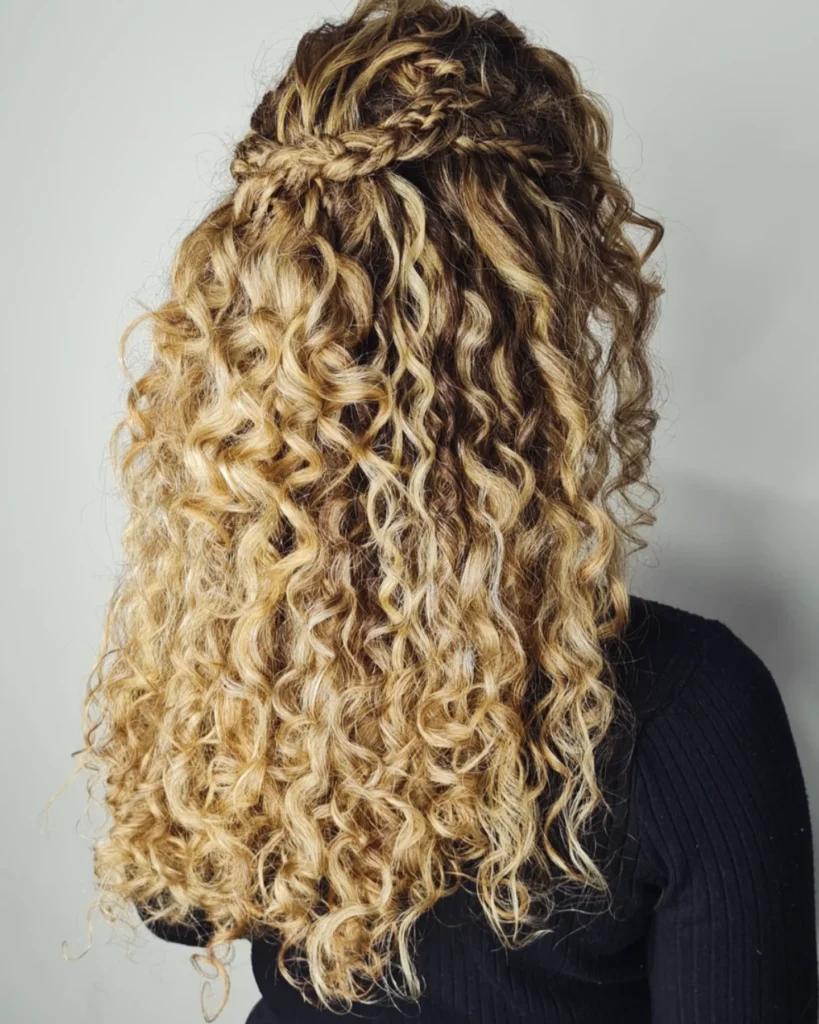 Long blonde curly hair styled in a braided half up hairstyle with loose defined curls flowing down the back.