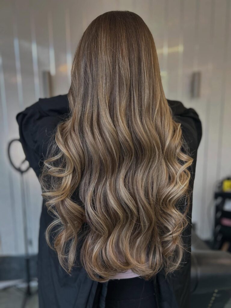 Long layered brunette hair styled in soft blowout waves with smooth volume and movement.