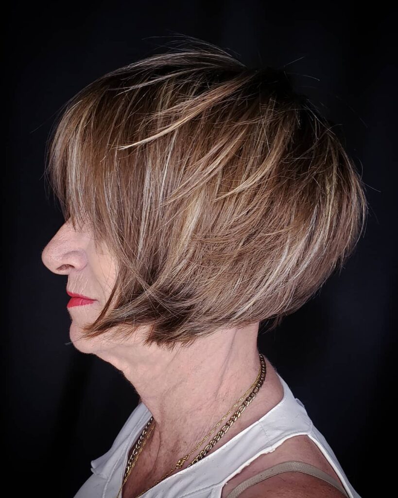 Short textured bob with stacked layers and side swept bangs in warm highlighted tones.
