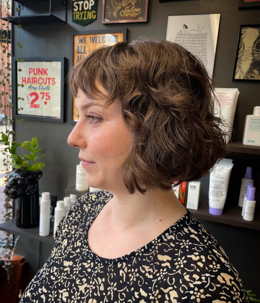 A woman with a textured curly bob and light wispy bangs in a natural medium brown color.