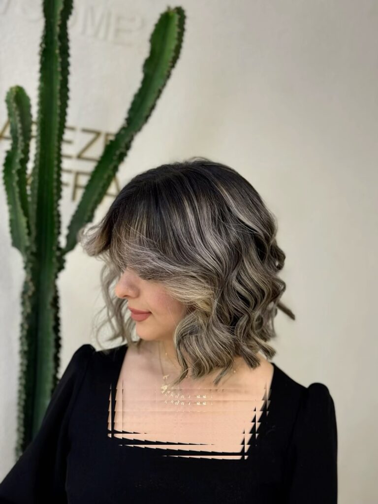 A woman with a wavy bob haircut and full blended bangs in a cool toned brunette and blonde color.