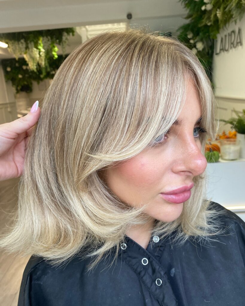 A soft layered blonde bob with curtain bangs and lightly flipped ends for a natural bouncy finish
