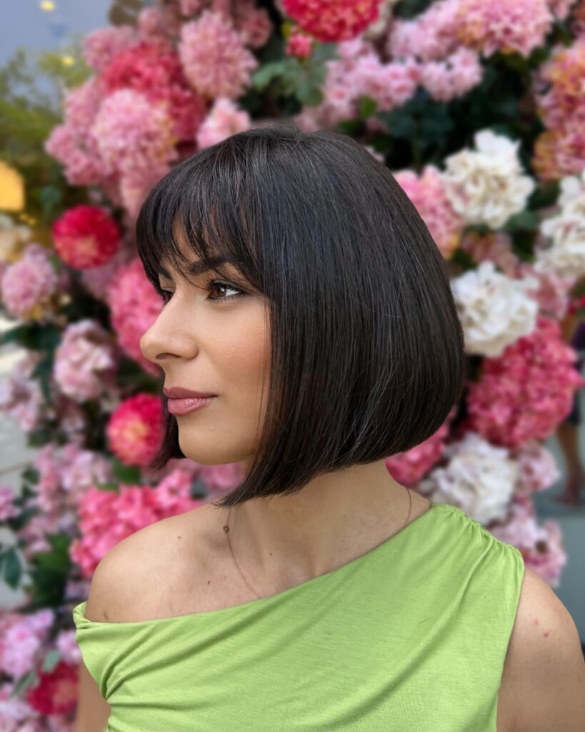 A sleek chin length dark bob with soft wispy bangs and a smooth polished texture