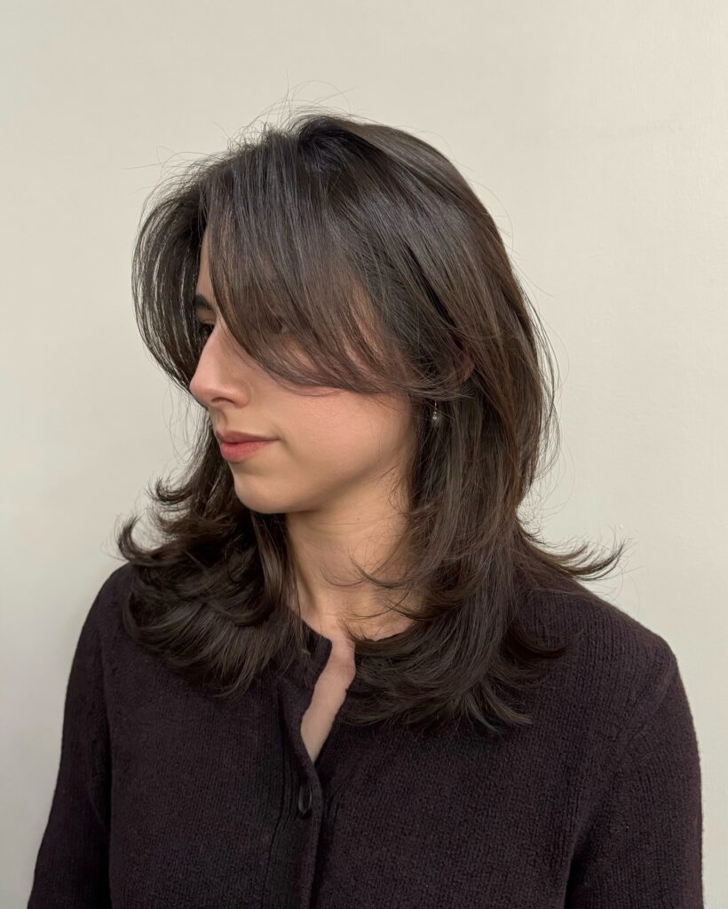 A feathered medium short brunette haircut with curtain bangs and softly flipped layered ends