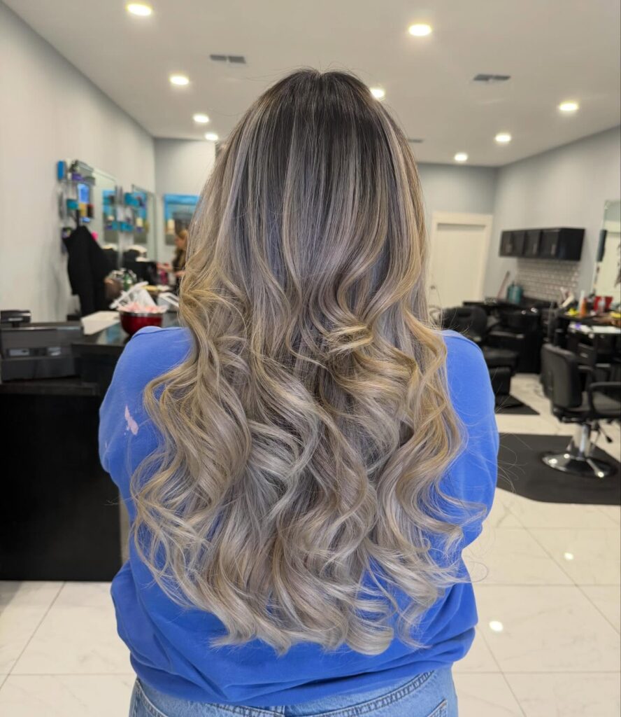 Long ash blonde hair with loose voluminous curls and blended layers in a salon styled finish.