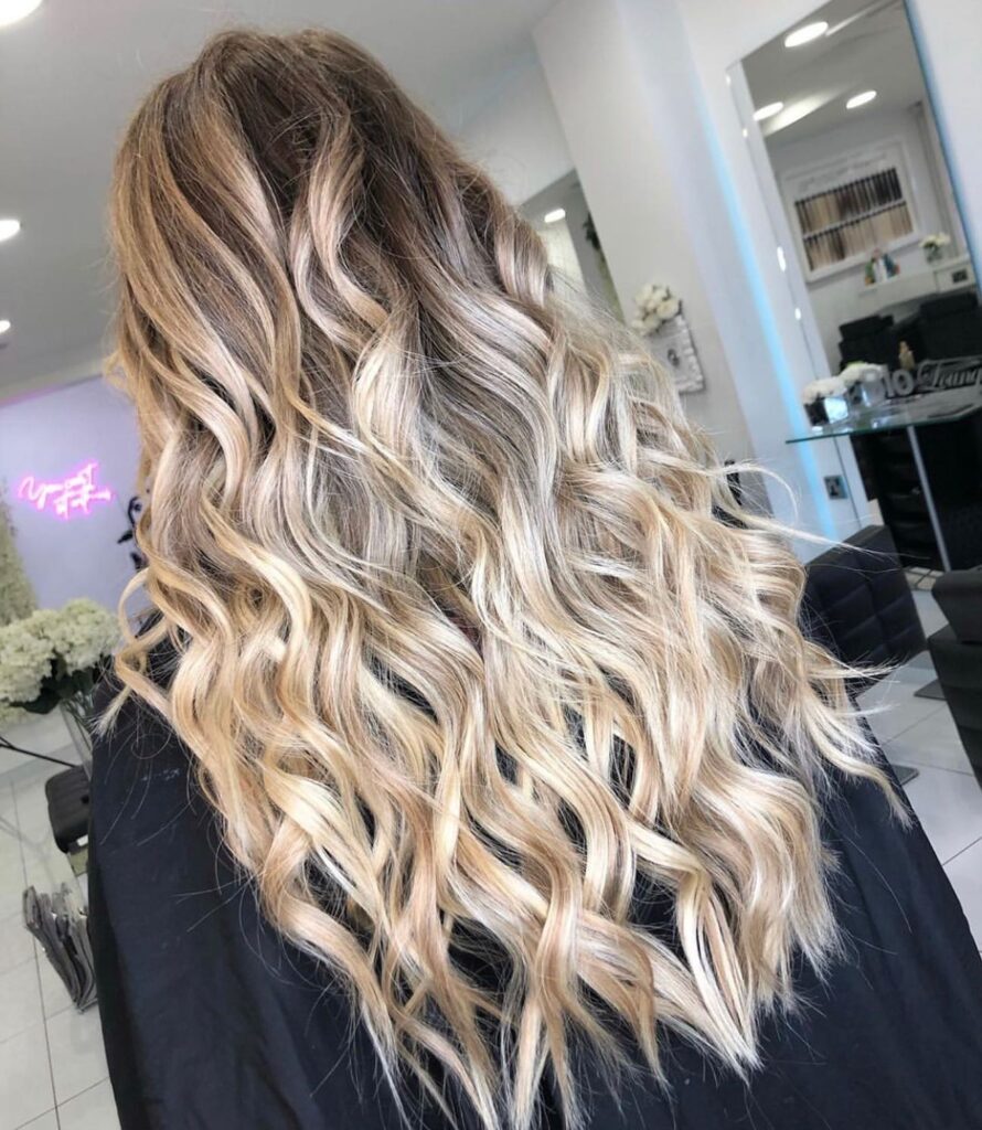 Long blonde balayage hair styled in loose beachy curls with a soft layered finish.