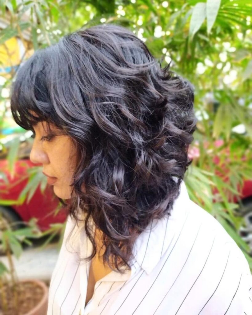 A voluminous dark curly lob with full blended bangs and soft layers.