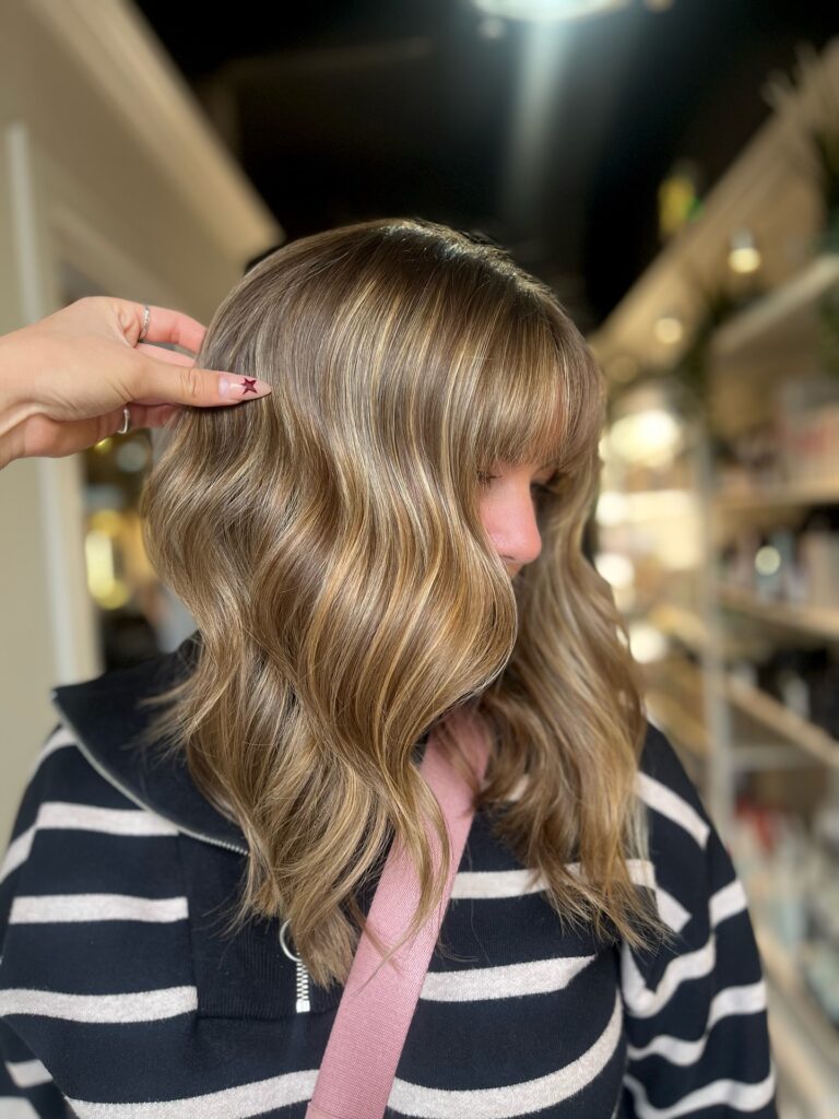 A wavy shoulder length lob with curtain bangs and warm brown tones.